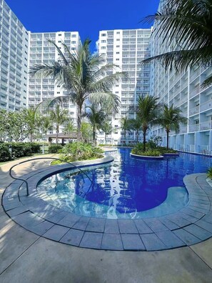 Ein Swimmingpool, umgeben von Palmen und modernen Apartmentgebäuden.