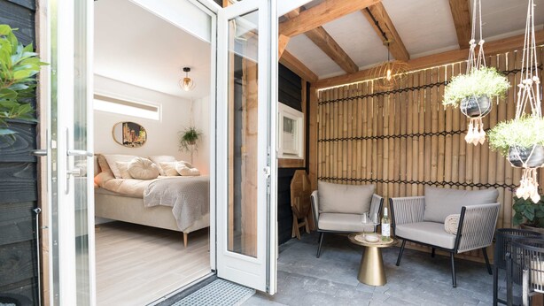 Puerta abierta que da a un dormitorio con cama, sofá y una mesita con una botella.