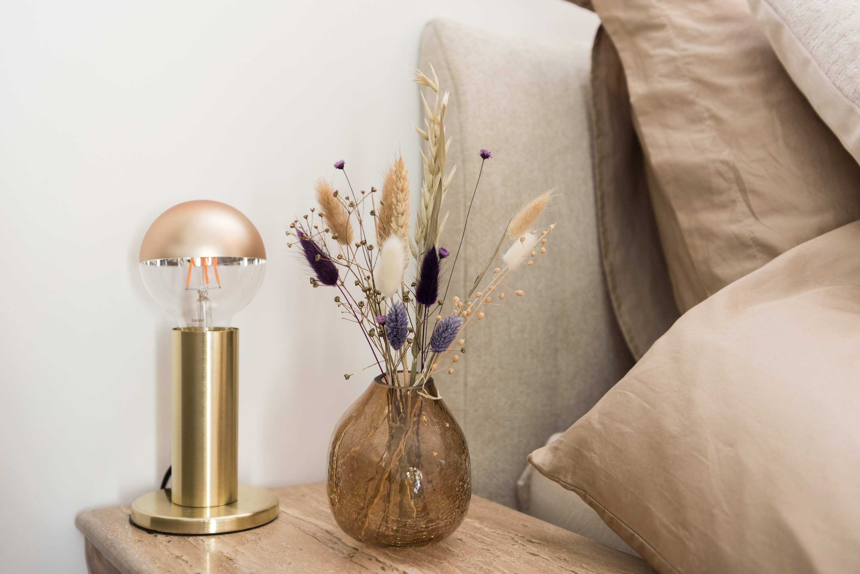 Une table de chevet avec une lampe et un vase de fleurs séchées.