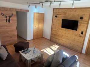 A modern living room with a wooden wall, a flat-screen TV, a sofa, a coffee table, and a decorative deer head. - Apartment Predigtstuhl for 2 persons, 50 sqm, balcony with unobstructed view of the mountains (Bad Reichenhall)