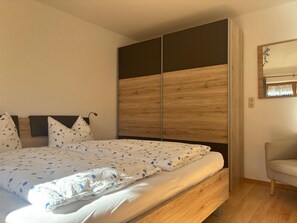 A bedroom with a bed, a wooden headboard, a chair, and a mirror on the wall. - Apartment Predigtstuhl for 2 persons, 50 sqm, balcony with unobstructed view of the mountains (Bad Reichenhall)