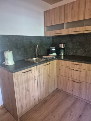 A kitchen with wooden cabinets, a black countertop, a coffee maker, and a toaster. - Apartment Predigtstuhl for 2 persons, 50 sqm, balcony with unobstructed view of the mountains (Bad Reichenhall)