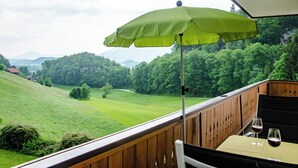 Un balcone con un ombrello verde, ringhiera in legno e un tavolo con bicchieri di vino.