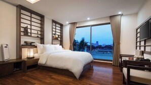 A modern hotel room with a large bed, a TV, a desk, and a view of the cityscape through the window. - MIBEE Hotel (Hanoi)