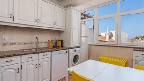 A kitchen with white cabinets, a washing machine, a sink, and a window with a view of buildings.