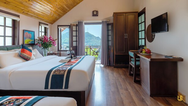 Una habitación de hotel con techo de madera, una cama con colcha estampada, un escritorio con frutero y un televisor montado en la pared.
