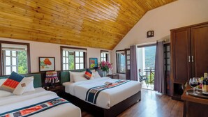 Habitación de hotel con dos camas, techo de madera, ventanas amplias y un balcón.
