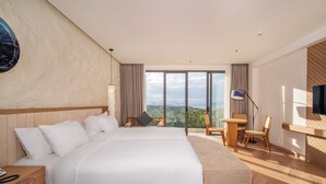 A modern hotel room with a large bed, a desk, and a chair. There is a TV mounted on the wall and a window with a view of the city.
