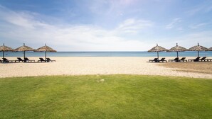 A beach with lounge chairs and thatched umbrellas.