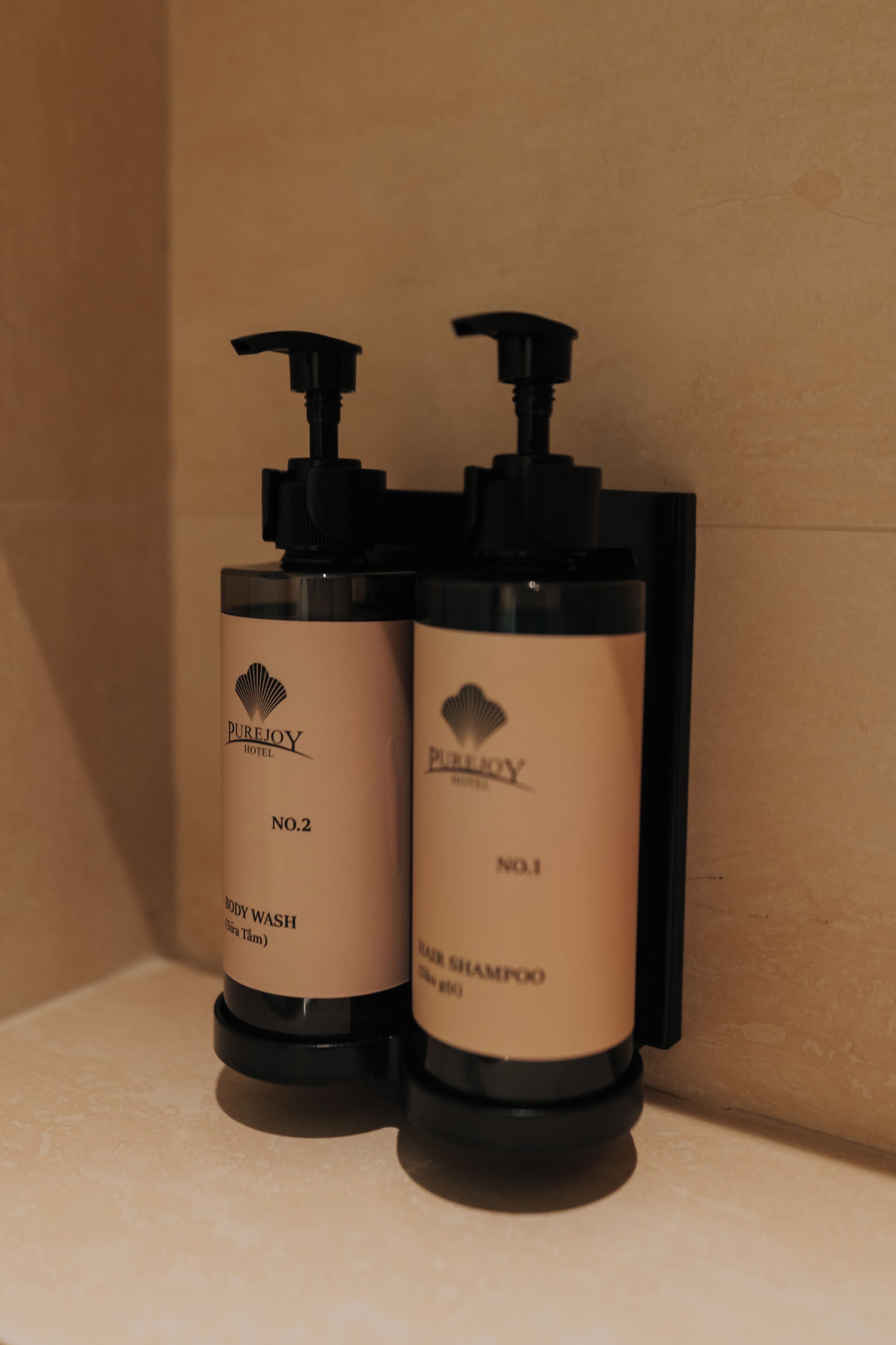 Two bottles of PureJoy Hotel body wash and shampoo on a shelf.