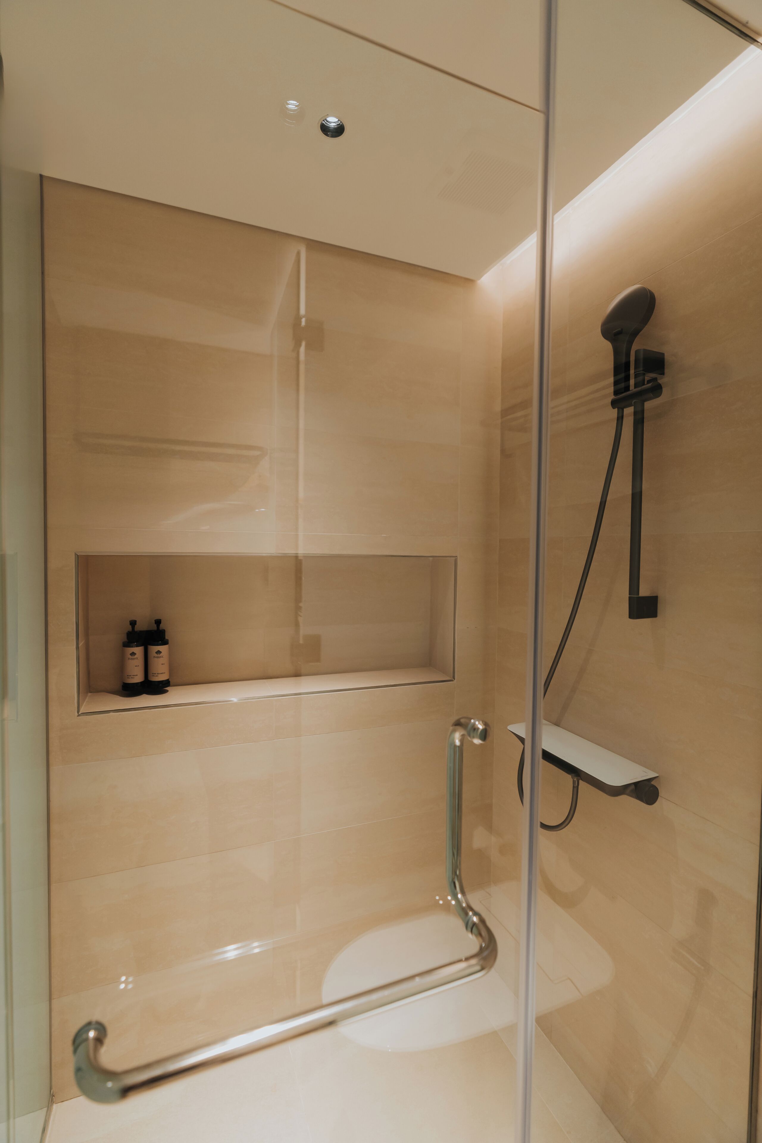 Une douche moderne avec un pare-douche en verre, une étagère pour les articles de toilette et une douchette à main.