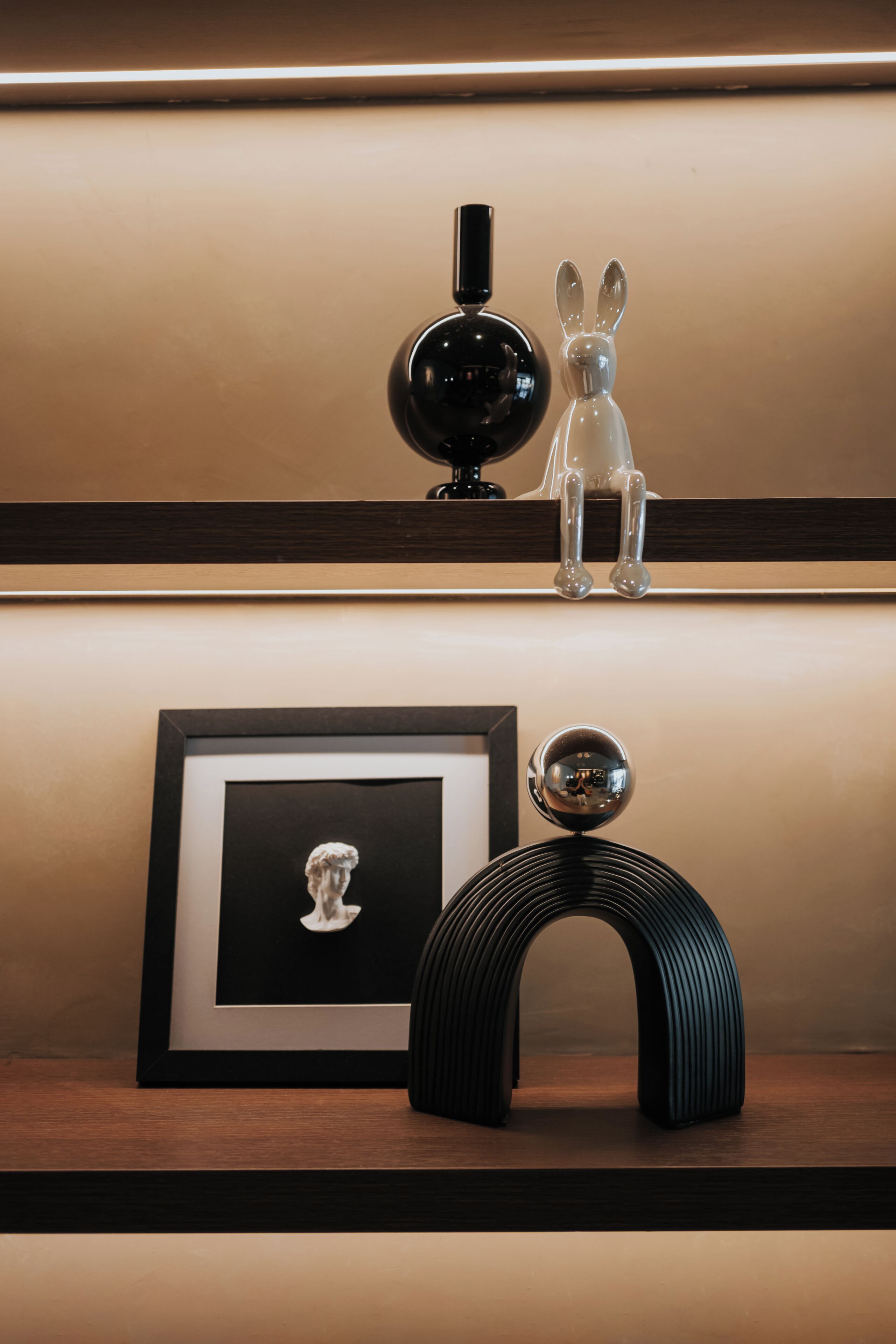 A framed bust sculpture, a black spherical object, and a clear glass sculpture on a shelf.