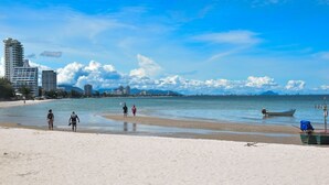 Une plage où l’on voit des gens se promener, un bateau et des bâtiments en arrière-plan.
