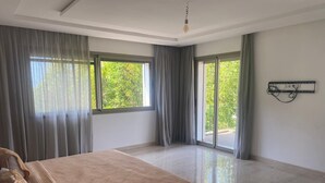 Une chambre spacieuse avec un grand lit, des portes-fenêtres coulissantes donnant sur un balcon et un luminaire moderne.