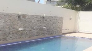 Une piscine rectangulaire avec un mur en pierre d’un côté et une zone de terrasse carrelée.