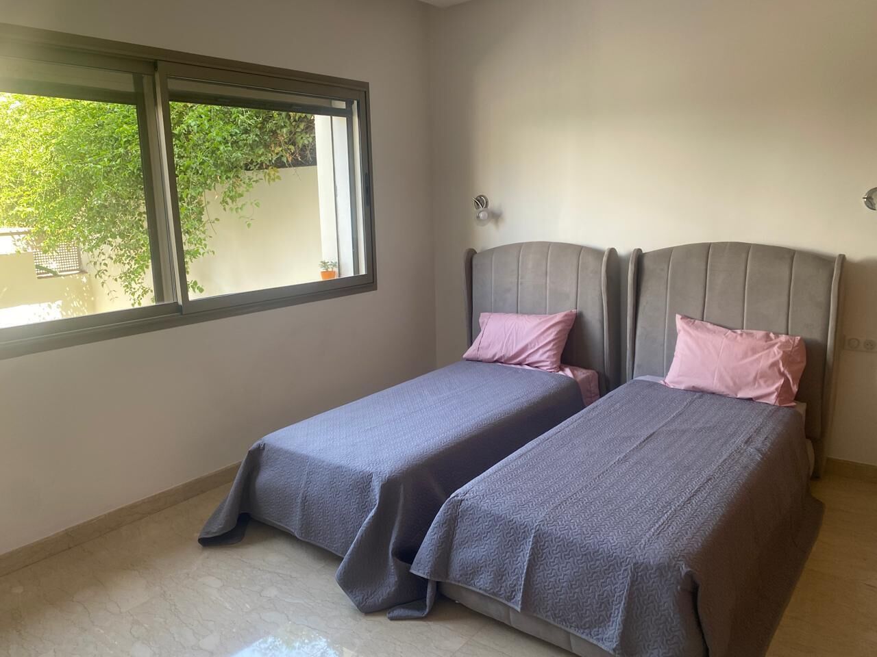 A bedroom with two beds, a window, and a view of greenery outside.