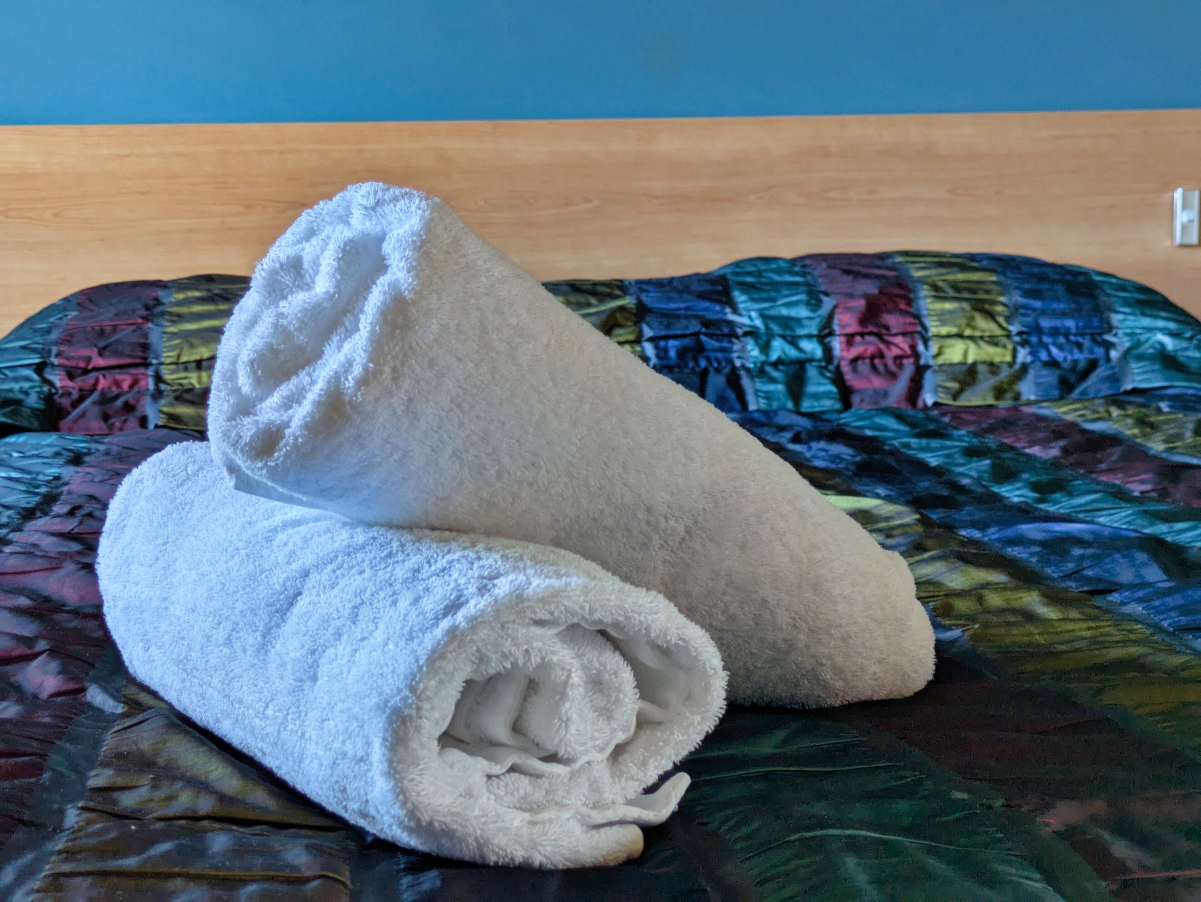 Un letto con una coperta colorata e due asciugamani bianchi piegati con cura.