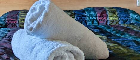 Un letto con una coperta colorata e due asciugamani bianchi piegati con cura.