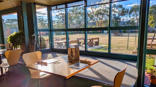 A modern indoor space with large windows offering a view of an outdoor area with picnic tables and greenery.