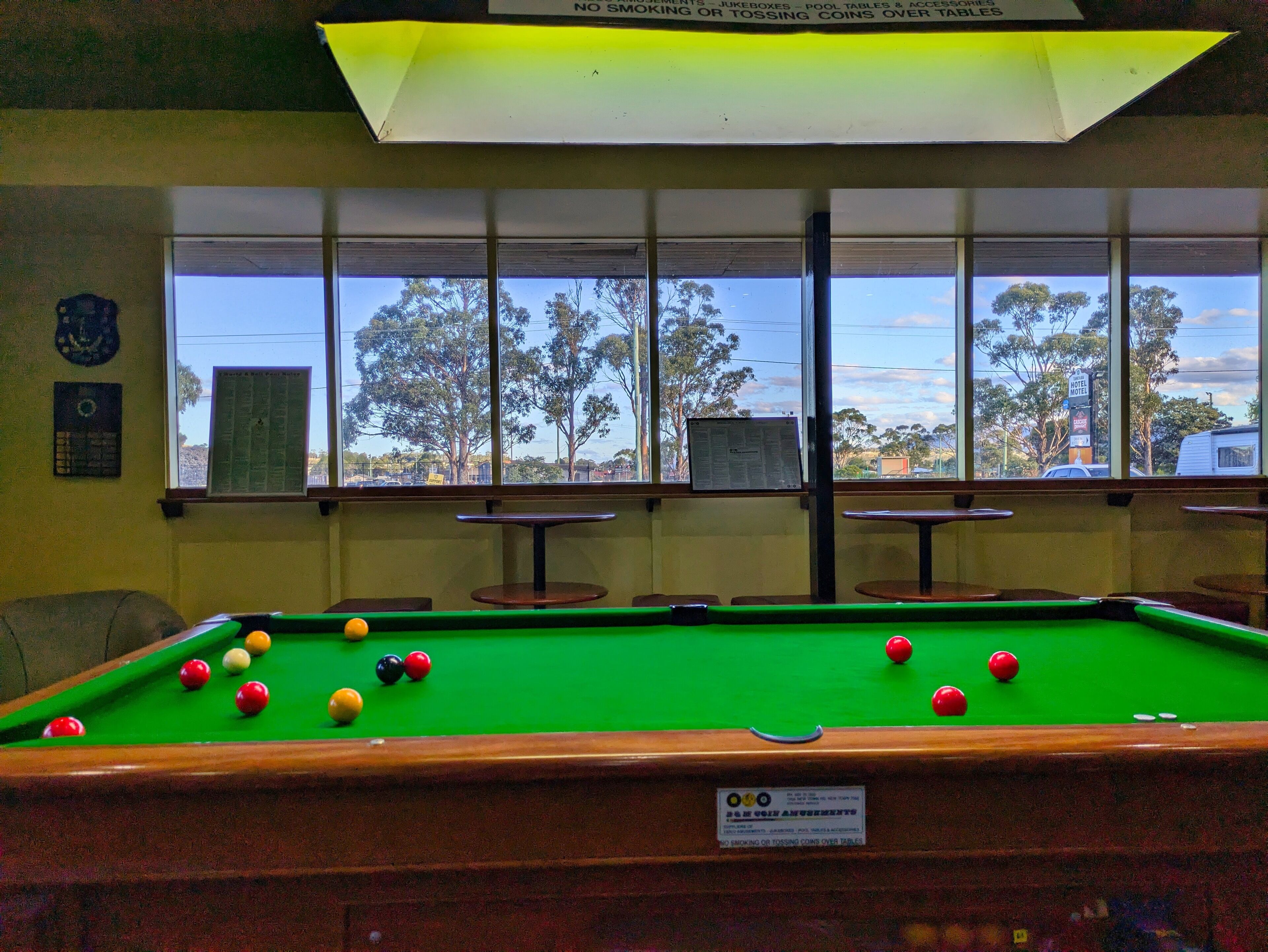 A pool table with balls, a window with a view of trees and a car, and a sign prohibiting smoking over tables.