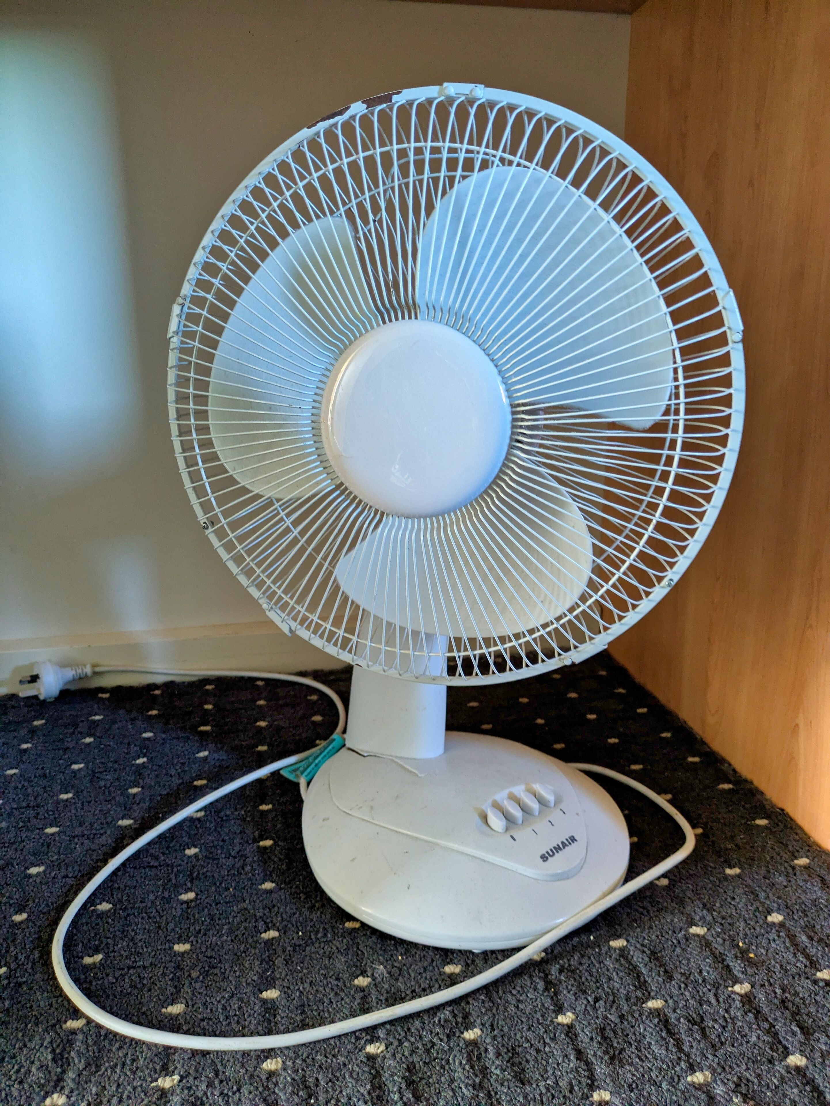 A white standing fan with a circular base and a power cord.