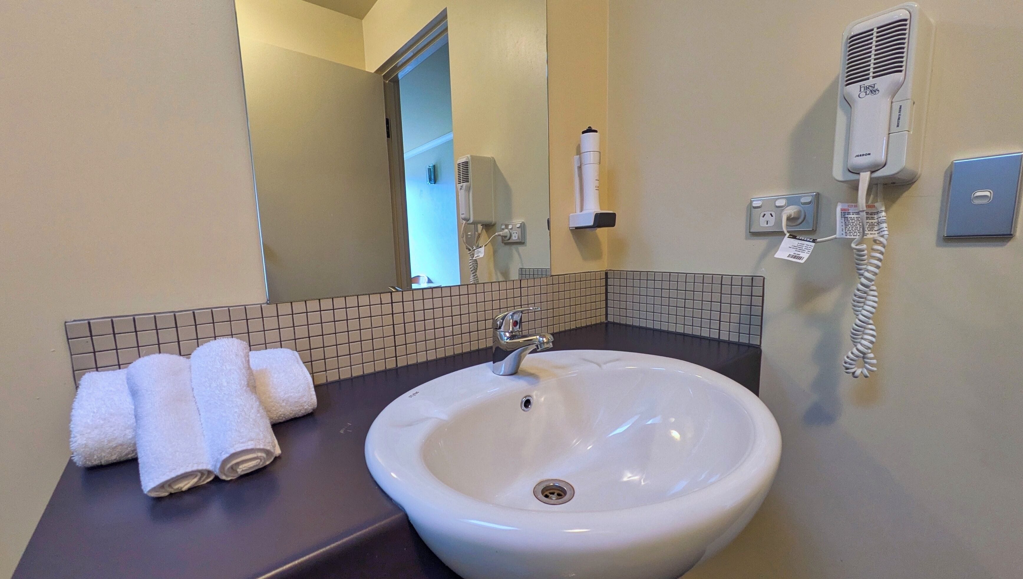 A bathroom with a white sink, a mirror, a towel rack with towels, a hairdryer, and a telephone.