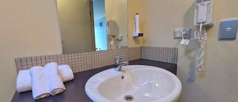 A bathroom with a white sink, a mirror, a towel rack with towels, a hairdryer, and a telephone.