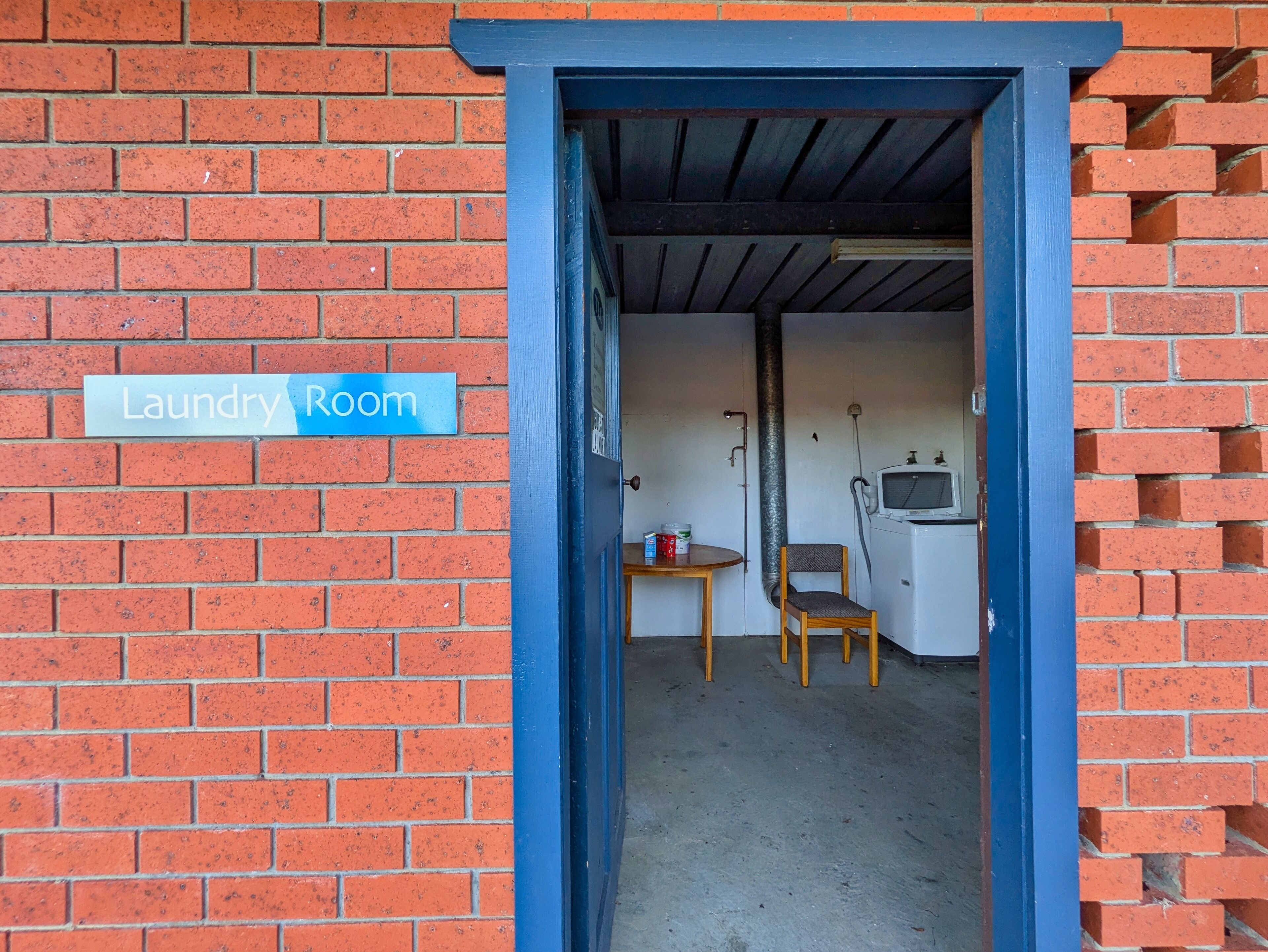 A laundry room with a sign, a washing machine, a chair, and a table.