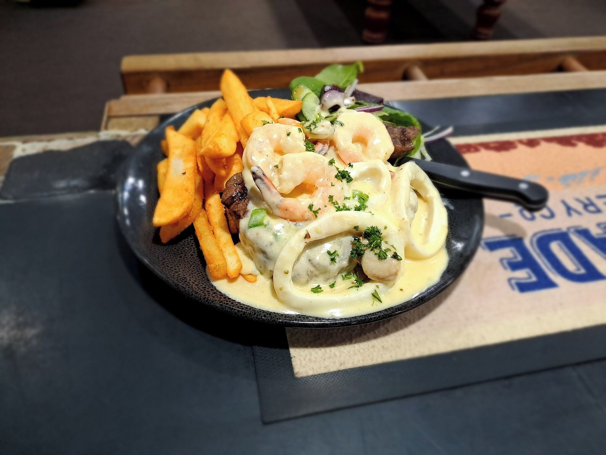 Un plato de comida con camarones, pasta y papas fritas sobre un plato negro.