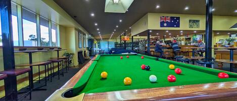 Une table de billard avec des billes, un coin bar et un drapeau accroché au mur.