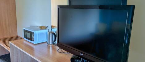 Habitación de hotel con escritorio de madera, televisor de pantalla plana, microondas, hervidor de agua y ventilador.