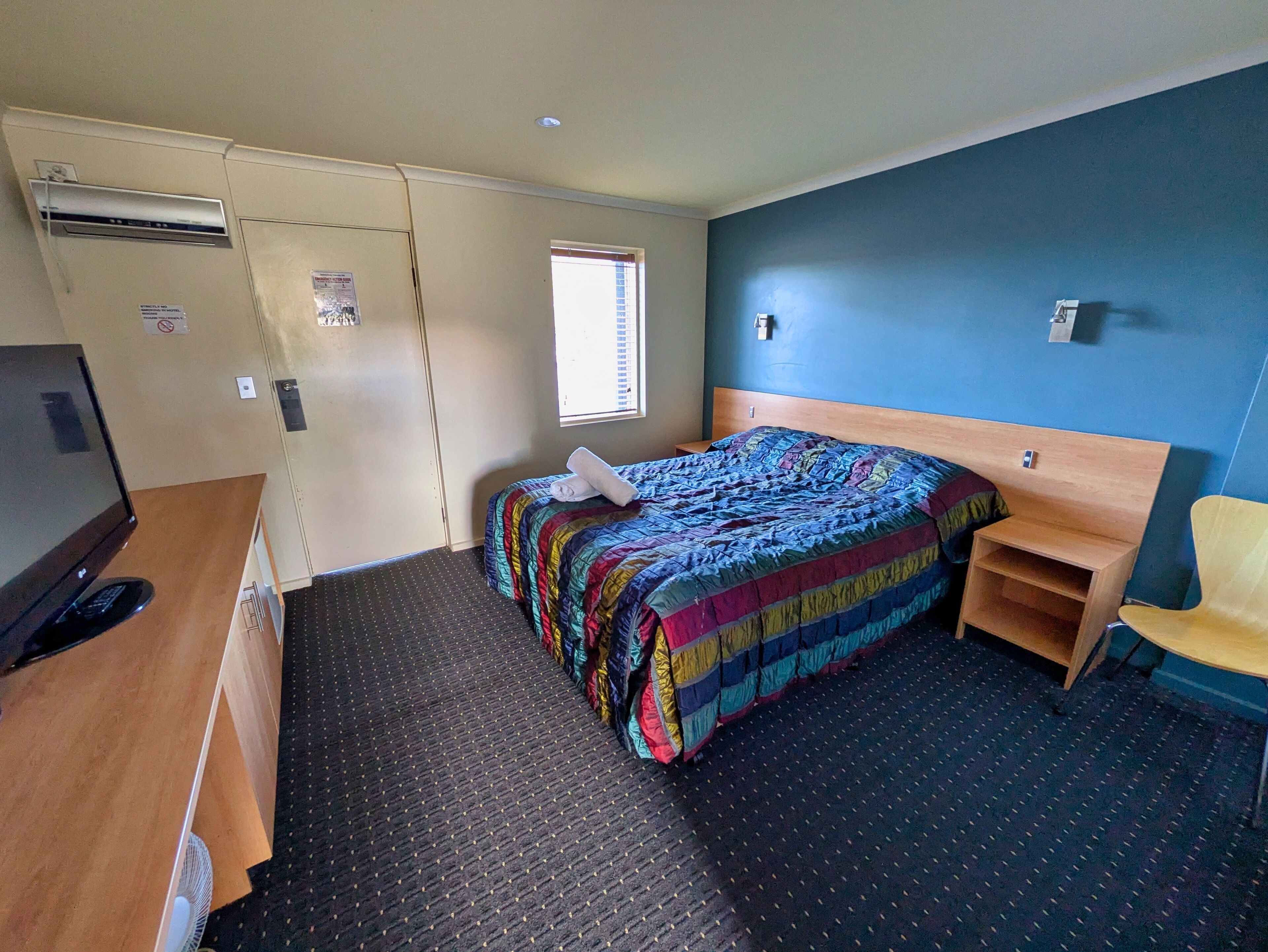 A compact hotel room with a bed, a desk, a chair, and a small window.