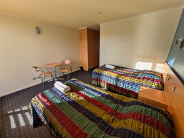 Habitación de hotel con dos camas, una mesita, dos sillas, un armario de madera y una ventana con persianas.