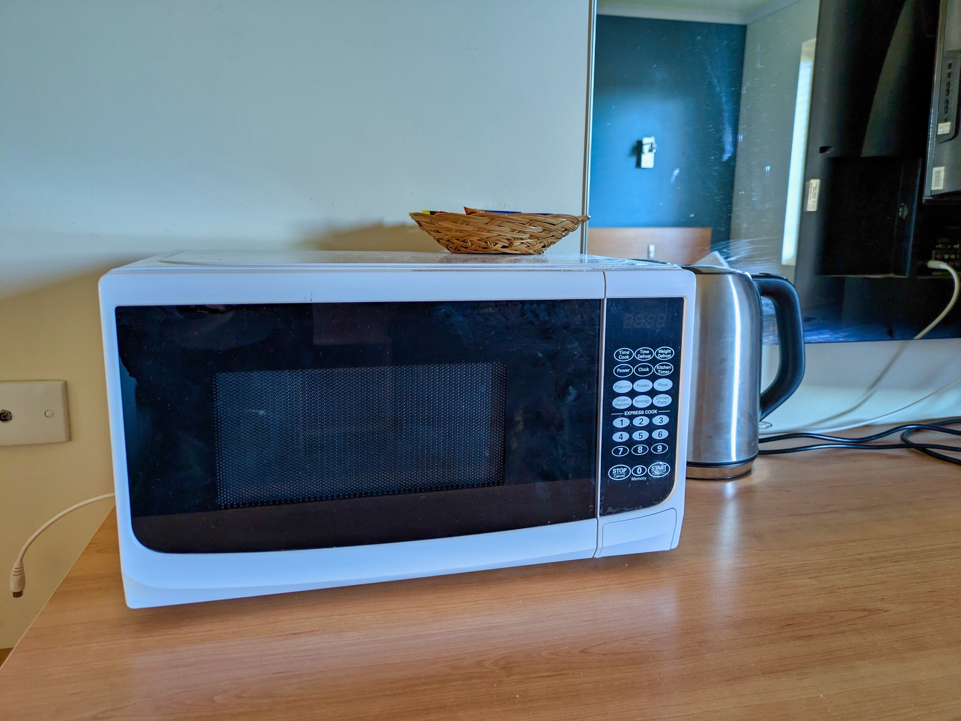 A white microwave on a wooden table with a basket on top.