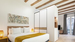 Une chambre moderne avec un grand lit, des poutres en bois, un téléviseur fixé au mur et une fenêtre avec des rideaux.