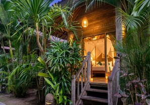 A wooden structure with a staircase leading to a room with a bed and a hanging light fixture. - Kama Nusa (Lembongan Island)
