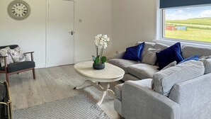 A modern living room with a grey sofa, a round coffee table, and a white door. - 3 bedroom accommodation in Hawick (Hawick)