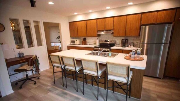 Une cuisine moderne avec des meubles en bois, un réfrigérateur en acier inoxydable, un grand îlot central doté de tabourets de bar et un four encastré.