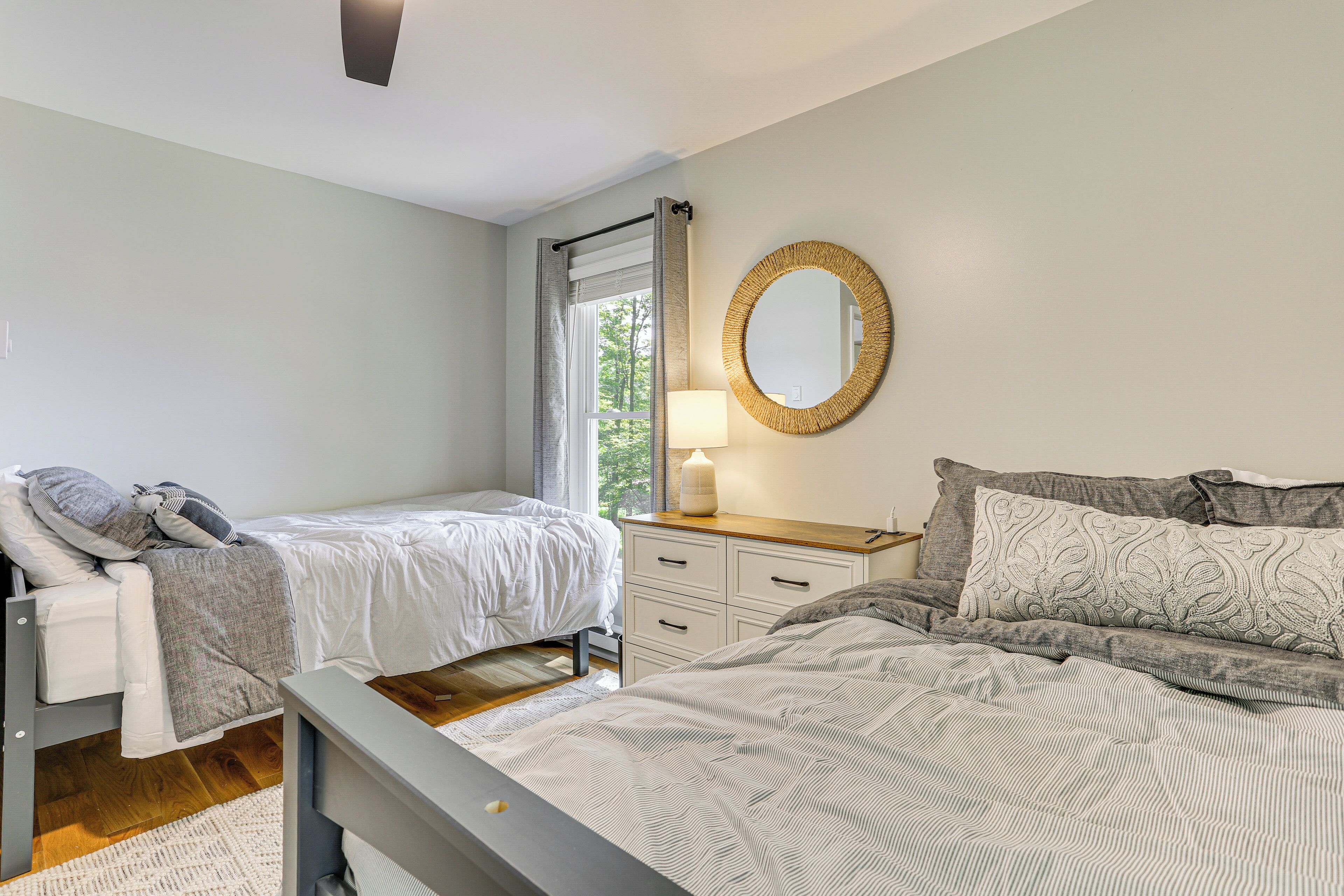 A bedroom with two beds, a bedside table with a lamp, a dresser, and a large mirror on the wall.