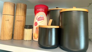 A shelf with salt and pepper shakers, a container of Nestle Coffee Mate, and two metal containers with lids. - Modern Downtown Suite - Walking Distance to Restaurants, Shops, & Grocery Stores (Golden)