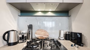 A modern kitchen with a gas stove, kettle, coffee maker, and a wooden cutting board.