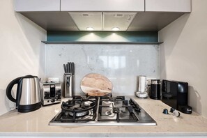Una cocina moderna con estufa a gas, hervidor, cafetera y tabla de cortar de madera.