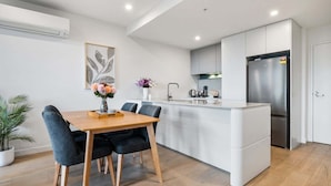 A modern kitchen with a central island, a dining area with a wooden table and chairs, and a built-in refrigerator.
