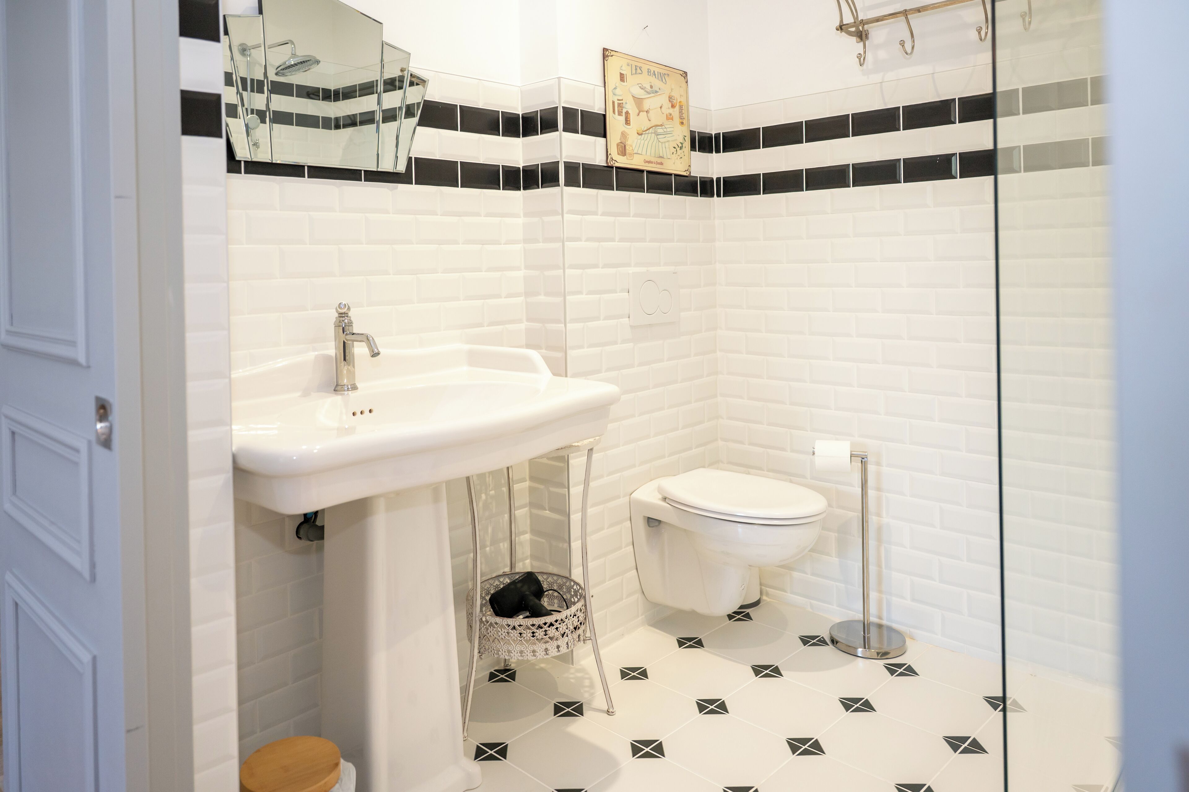 A bathroom with a white sink, toilet, and bidet, tiled floor with geometric patterns, and a small basket under the sink.