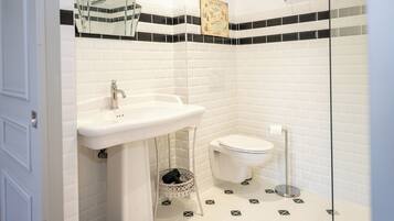 A bathroom with a white sink, toilet, and bidet, tiled floor with geometric patterns, and a small basket under the sink.