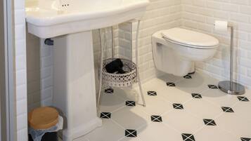 A bathroom with a white sink, toilet, and a small trash bin.