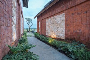 A pathway flanked by red brick walls with intricate carvings, leading to a building with a large carved panel.