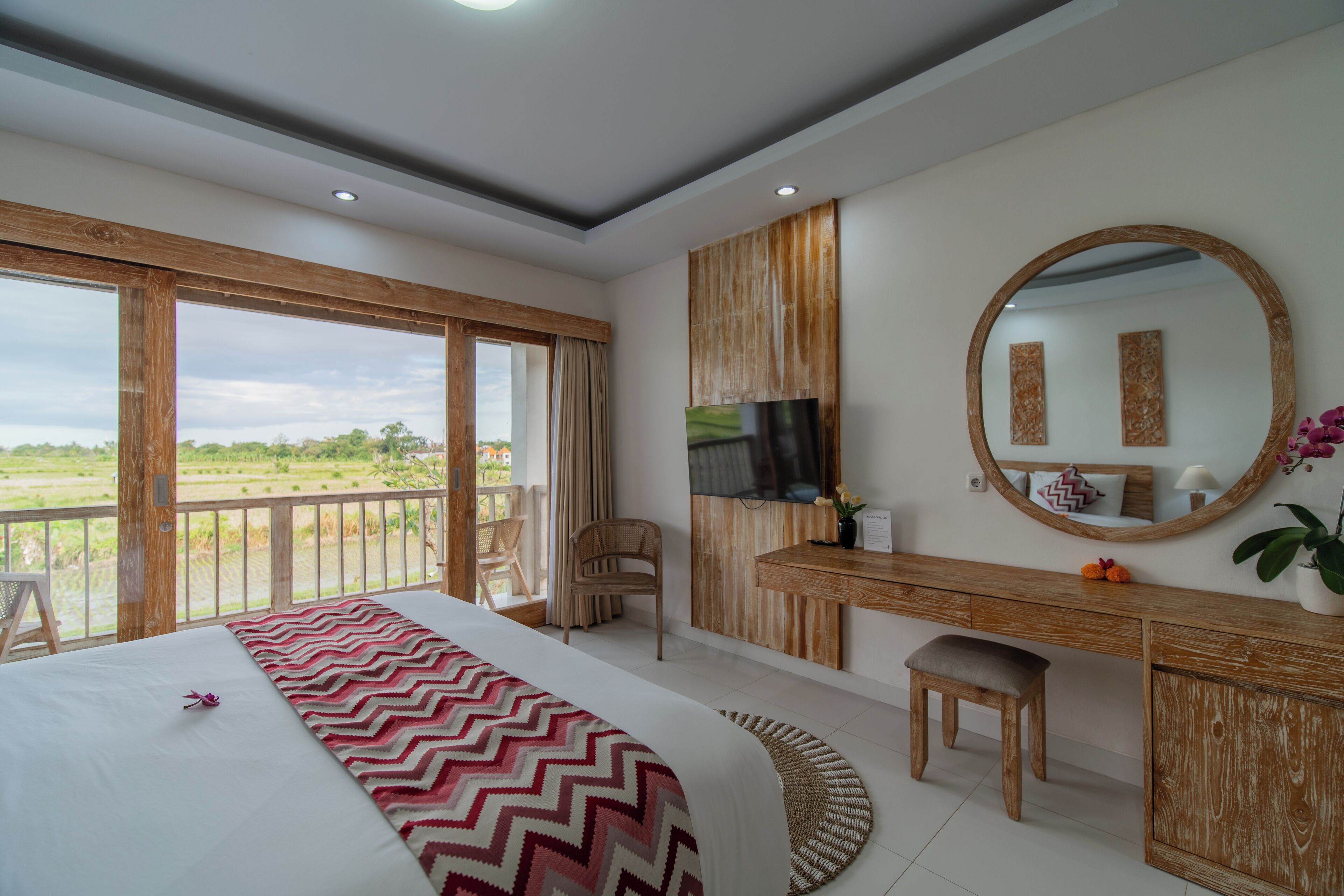 Ein Schlafzimmer mit einem großen Bett, einem Holztisch, einem Fernseher und einem Balkon mit Blick auf die Landschaft.