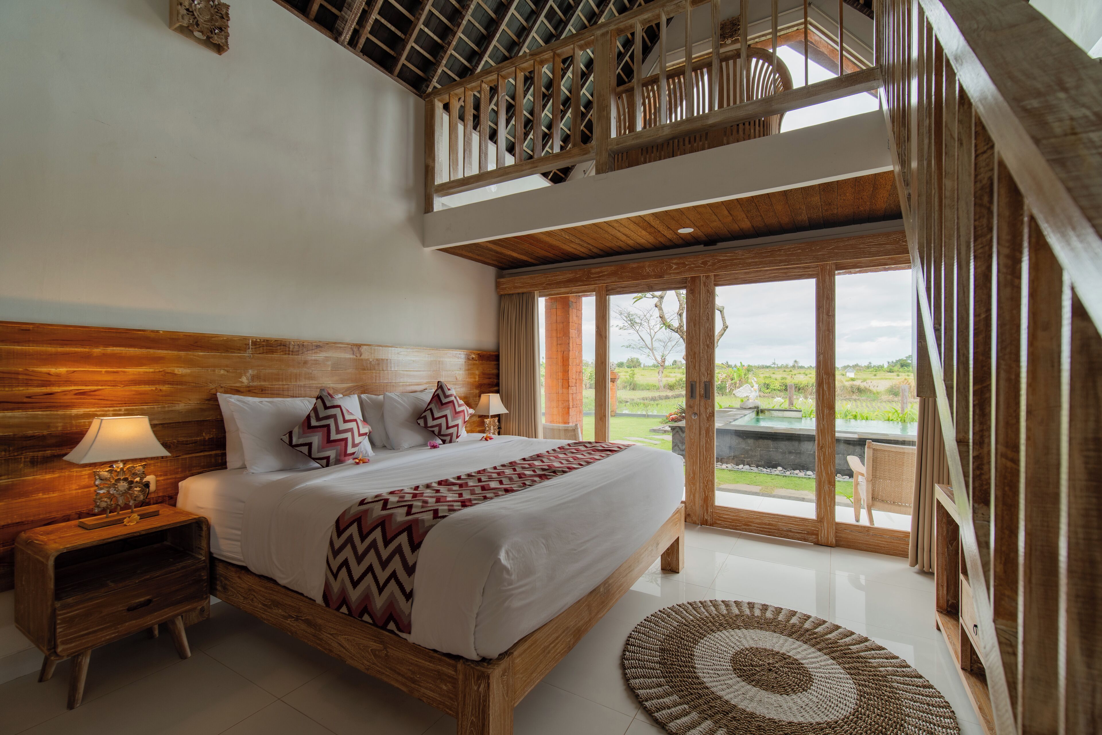 Ein geräumiges Schlafzimmer mit einem großen Bett, einem Holz-Kopfteil und Blick auf einen Garten durch eine Glastür.