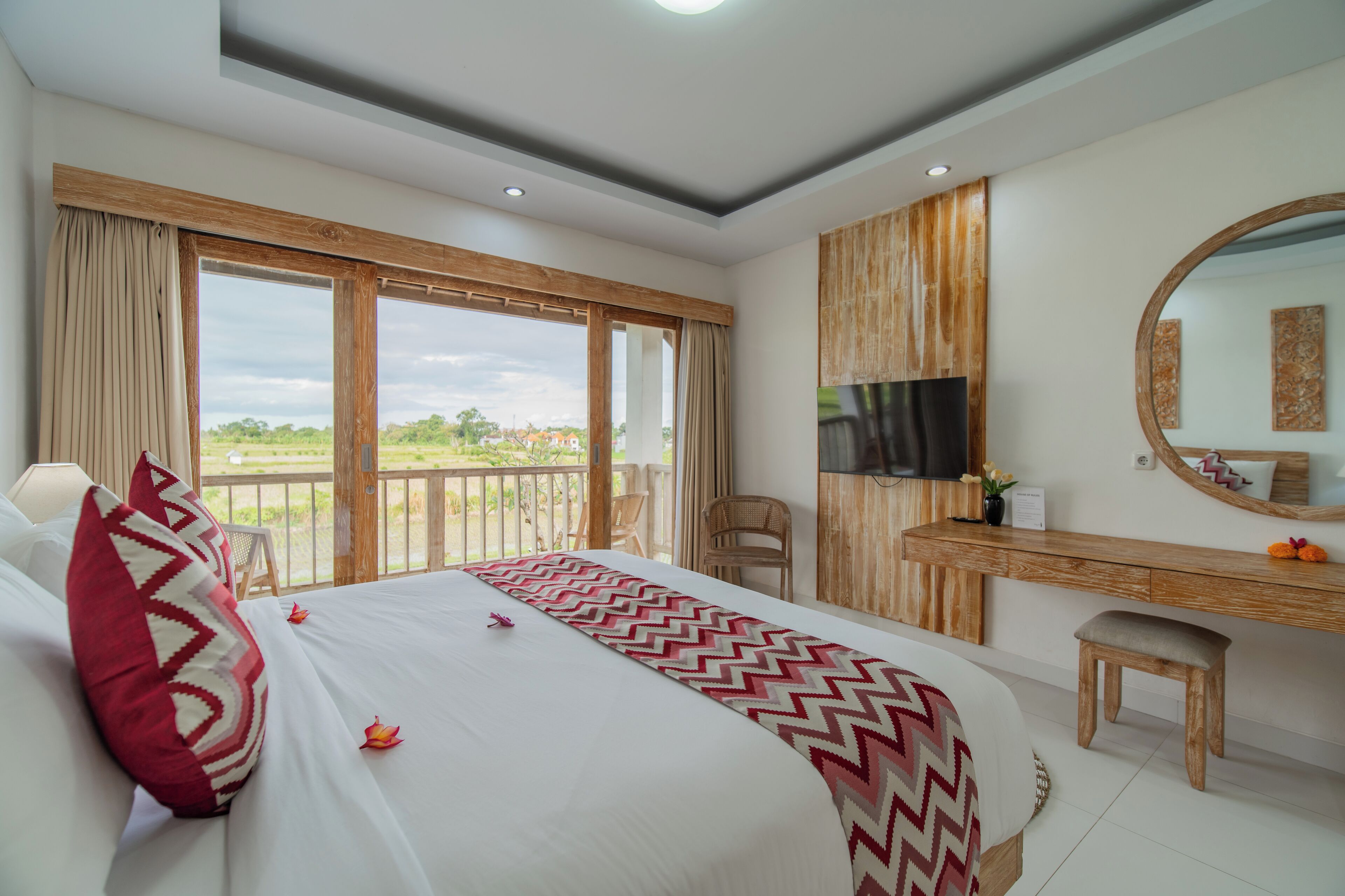 Habitación de hotel con una cama grande, un escritorio de madera, un televisor y un balcón con vistas.